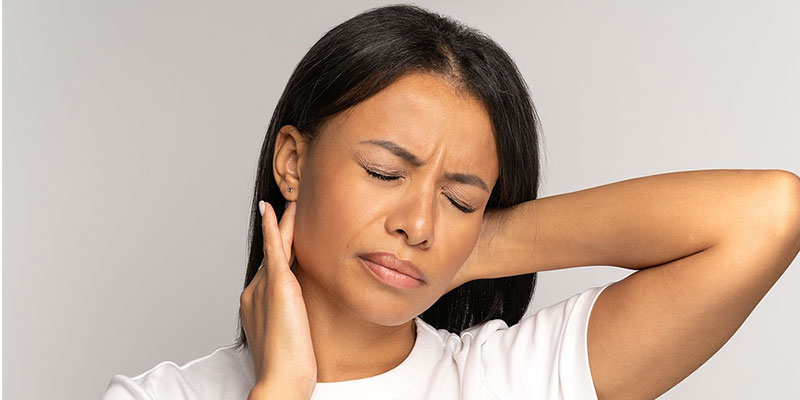 Woman grimacing in pain grabbing the back of her neck with a pinched nerve in Coralville, IA