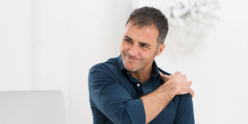 Man wincing in pain and grasping his shoulder pain in Coralville IA